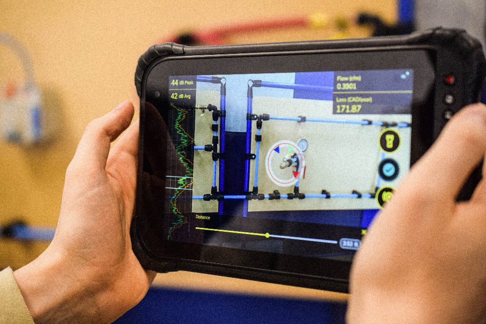 A person is using the PROSARIS app, connected to an ultrasonic sensor, to visually locate a compressed air leak.