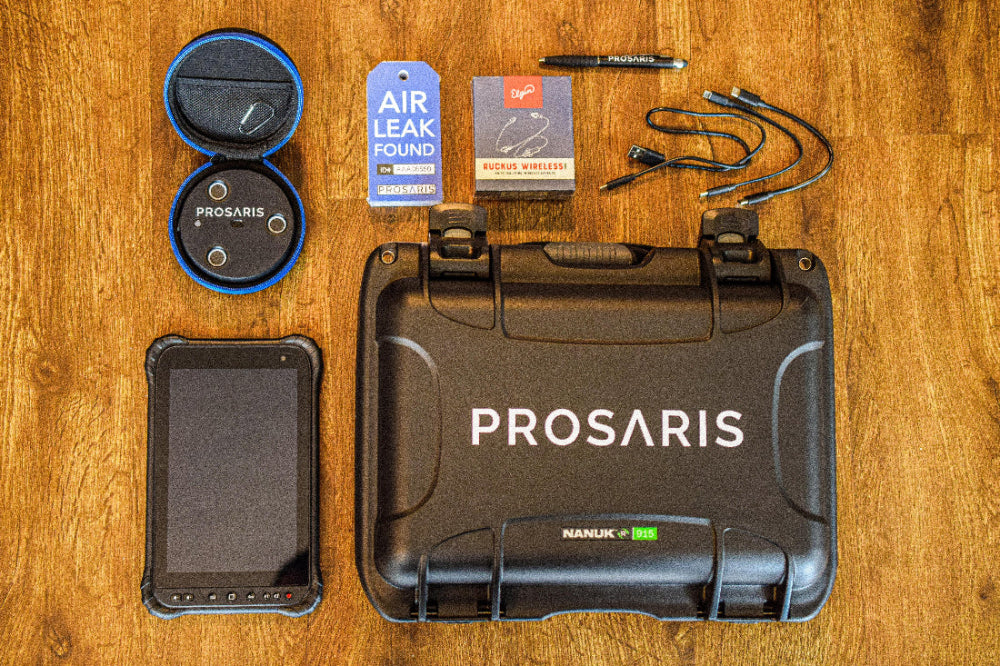 Displayed on a wood backdrop are all items included in an OL2 Pro Kit. The following items are a nOL2 device, OL2 carry case, NANUK hard case, tablet, connection & charge cords, wireless earbuds, Smart Tags, and pen.