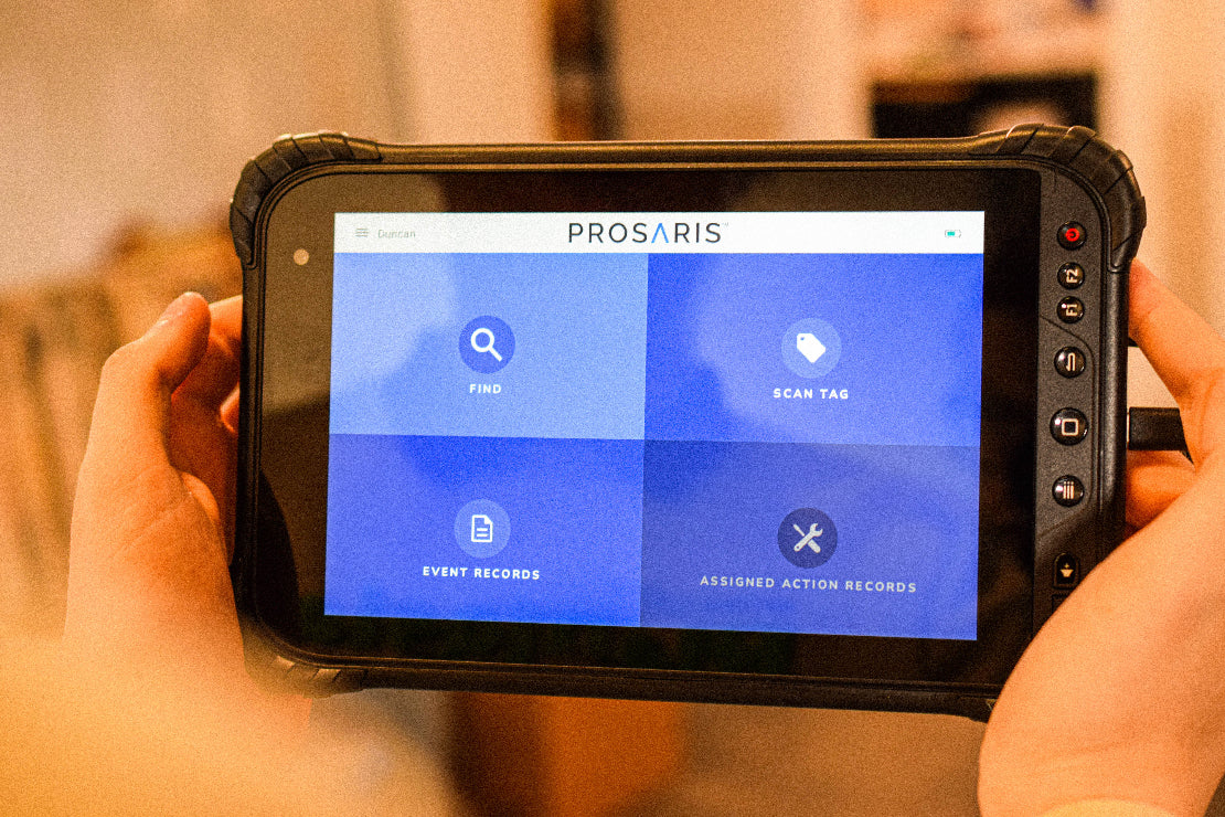 A person is holding a tablet that is displaying the App's home screen. Options to Find a leak, Scan a tag, view event records, and view assigned action records are on-screen.